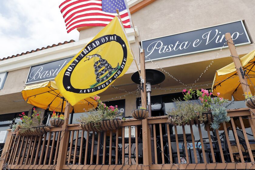 A Gadsden flag is hung with the flag of the United States of America at BasilicoOs Pasta e Vino in Huntington Beach on Tuesday. The restaurant has created some controversy with its an anti-mask policy.
