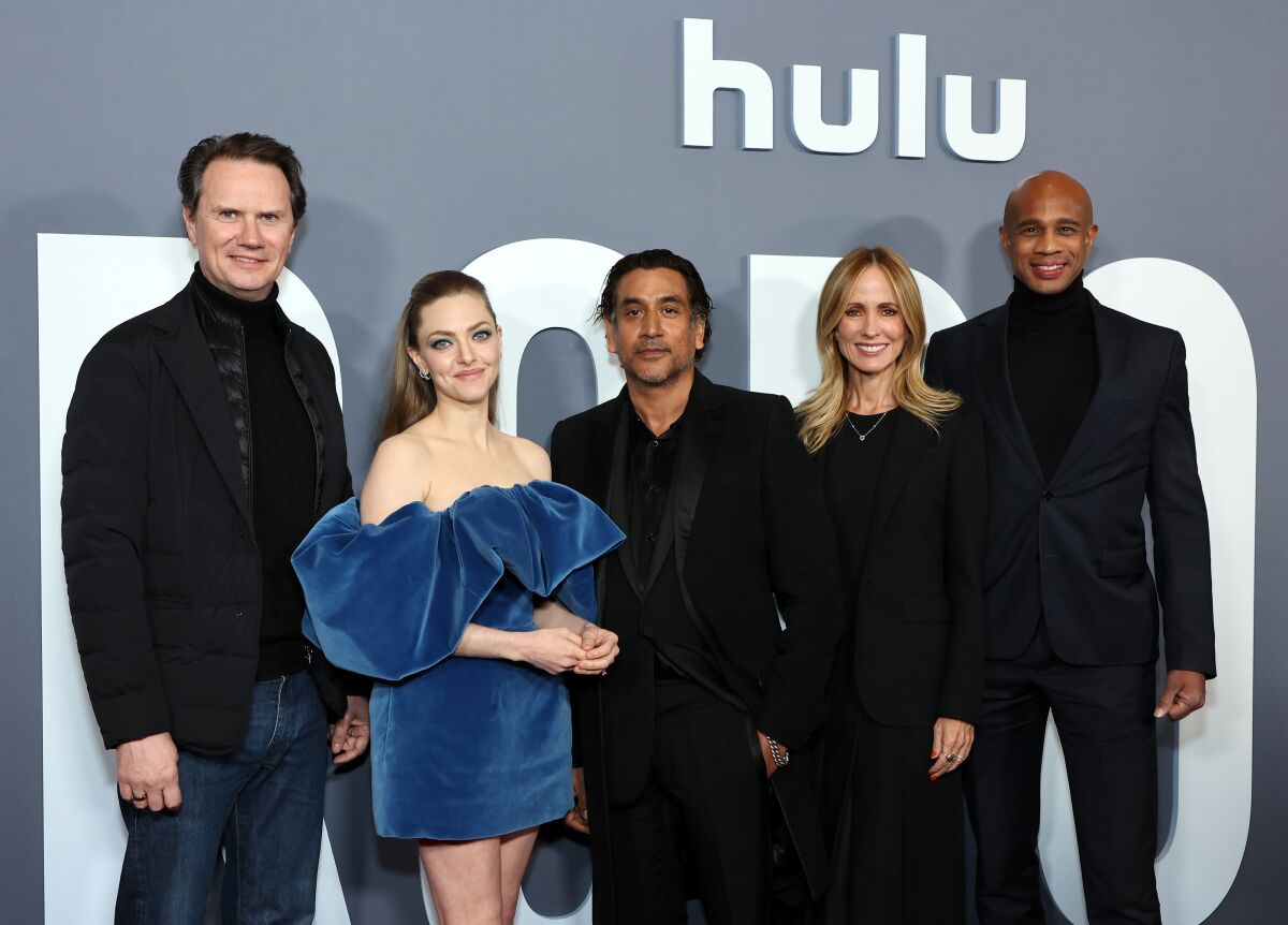 Three men and two woman stand in front of the Hulu logo on a wall.
