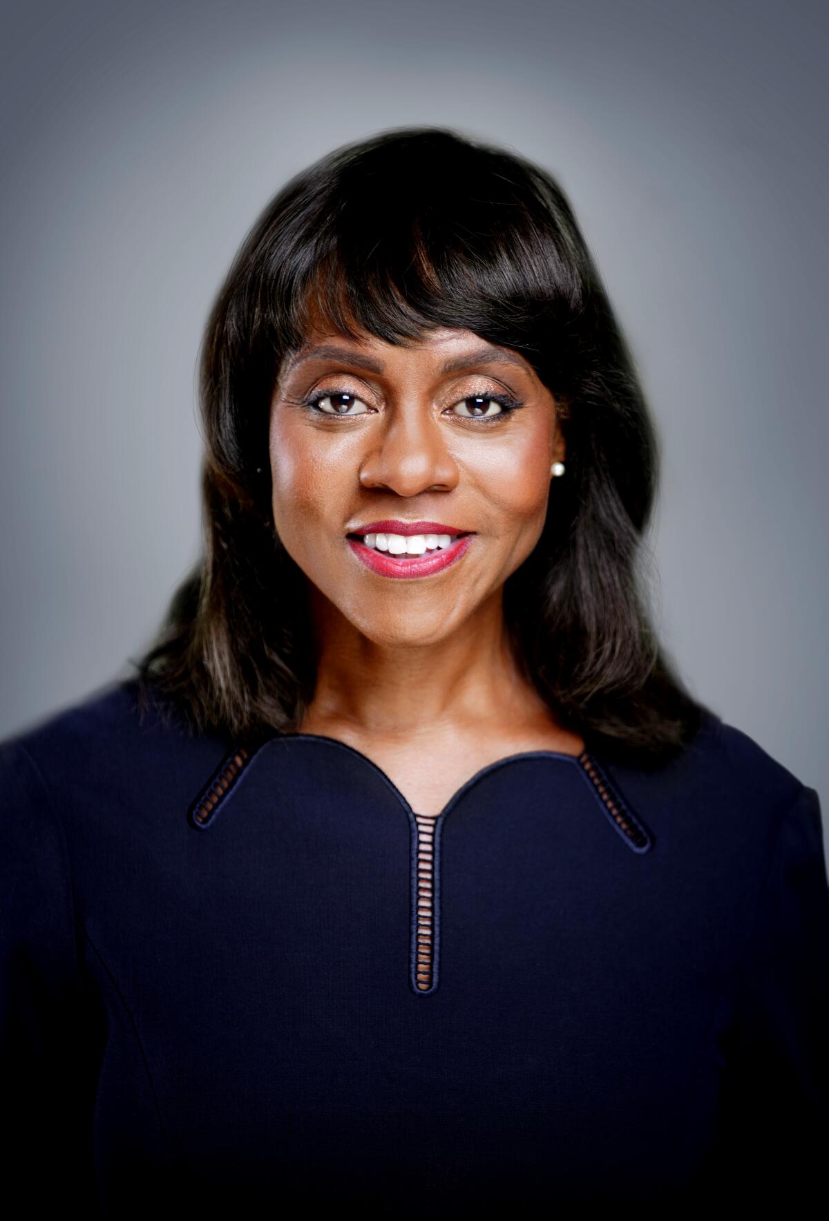 A headshot of Wonya Lucas, a woman with black hair wearing bright lipstick and stud earrings.