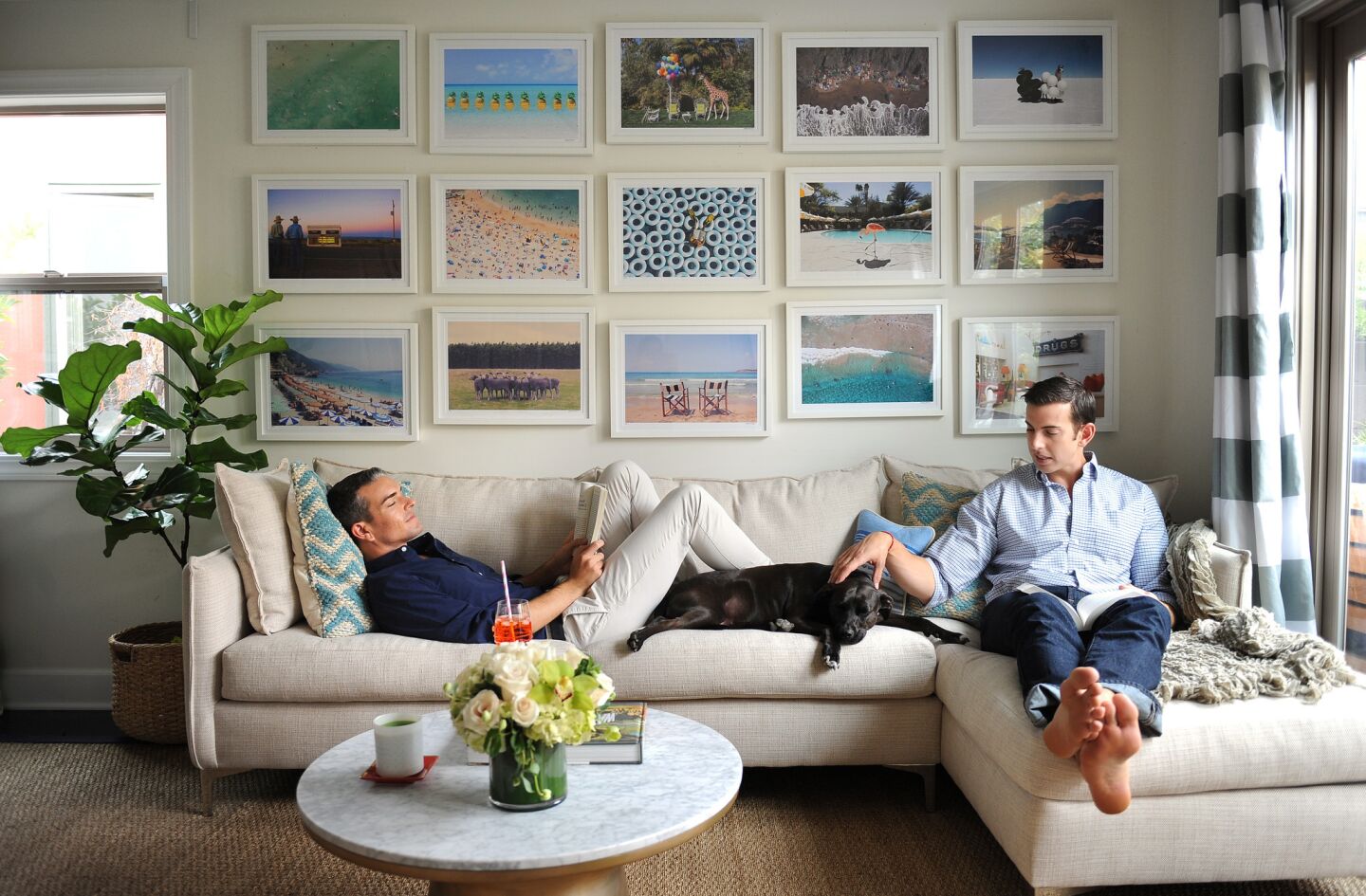 Gray Malin, left, Jeff Richardson and Stella kick back on a sectional sofa from the Joneses L.A. The curtains are from Pottery Barn, the table from West Elm and the fiddle leaf fig tree from Mickey Hargitay Plants. The photographs are Malin's.