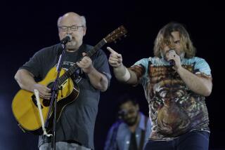 Kyle Gass closes his eyes while playing guitar and Jack Black points while singing next to him