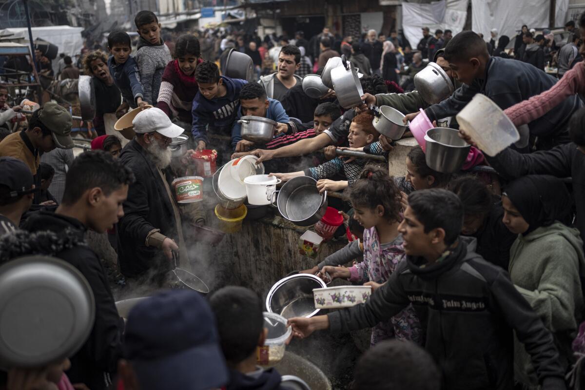 Palestinians holding out pots and containers at a meal distribution site