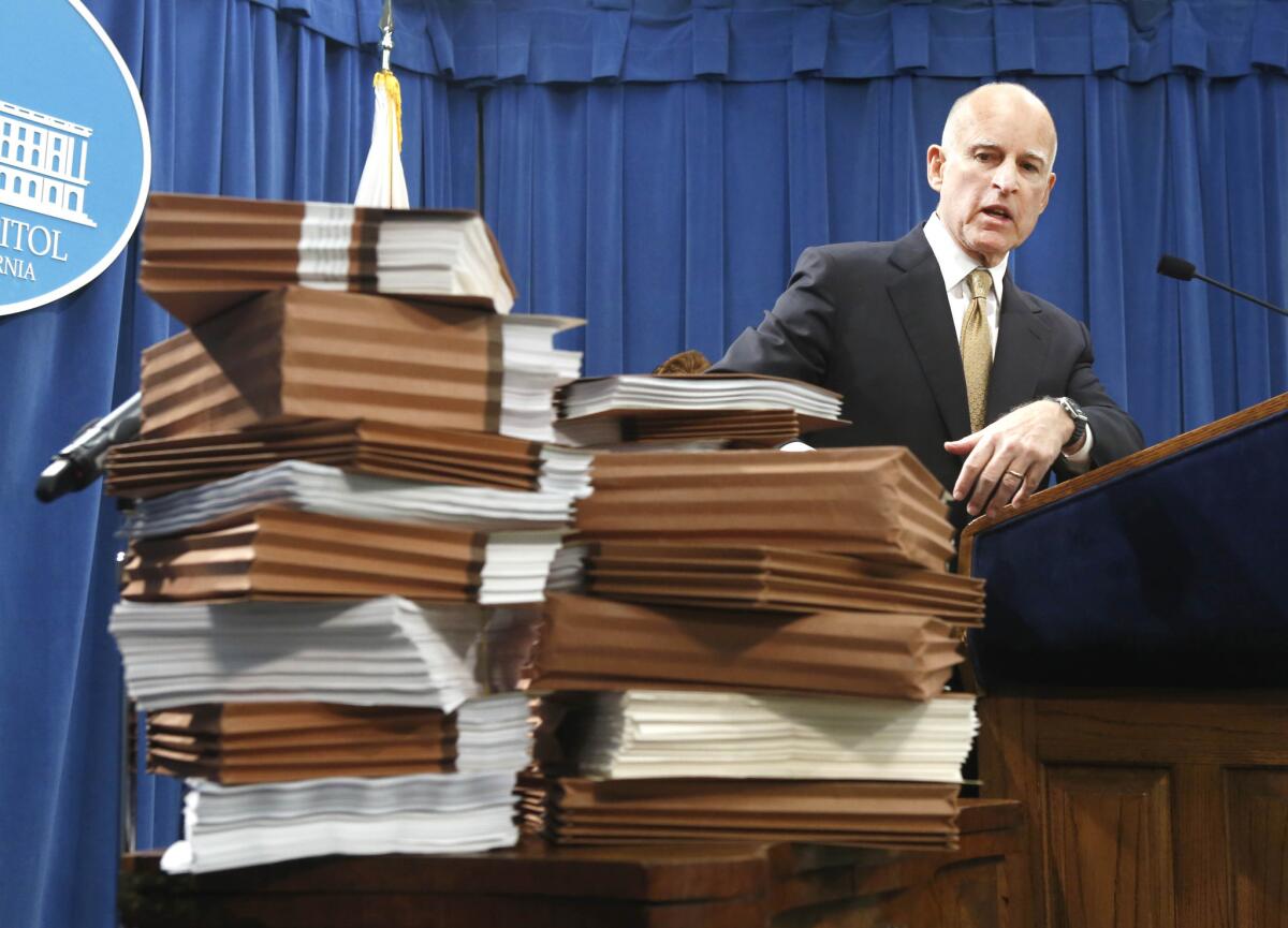 Gov. Jerry Brown gestures to a stack of reports on California prisons as he discusses his call for federal judges to return control of California prison to the state.