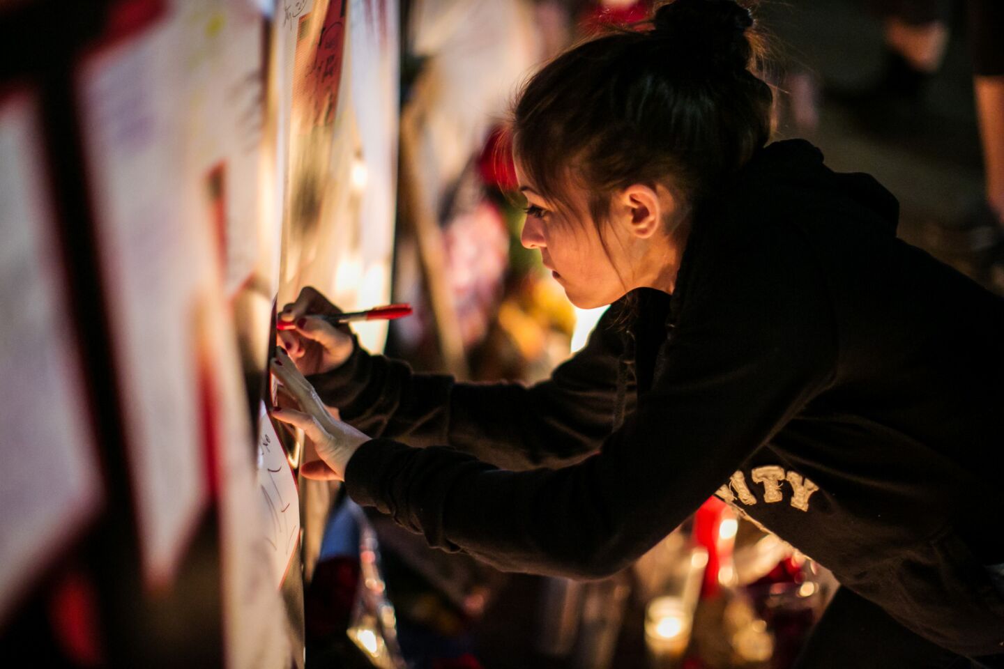 Claudia Zaragoza writes a message on a banner at the ever-growing memorial site to the victims of the recent mass shootings near the Inland Regional Center.