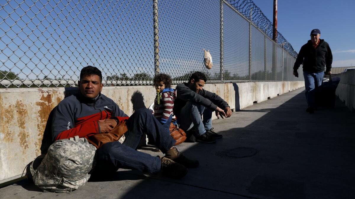 Asylum seekers Elvis Gonzalez Rodriguez, 23, left, of Havana and Robert Richard Braganca of Rio de Janeiro, with his toddler son, Mario, wait on the Matamoros and Brownsville International Bridge in Matamoros, Mexico.
