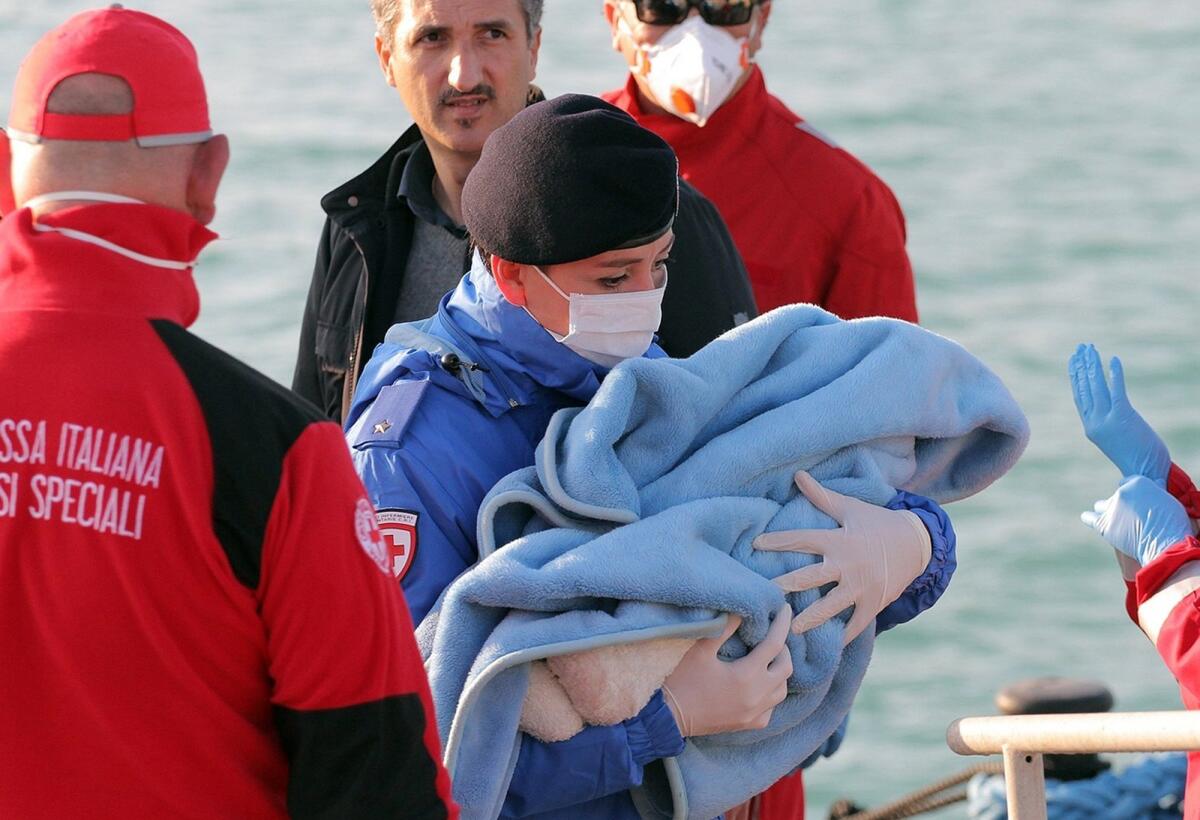 A Red Cross volunteer carries a baby wrapped in a blanket after migrants disembarked at the Sicilian Porto Empedocle harbor, Italy.