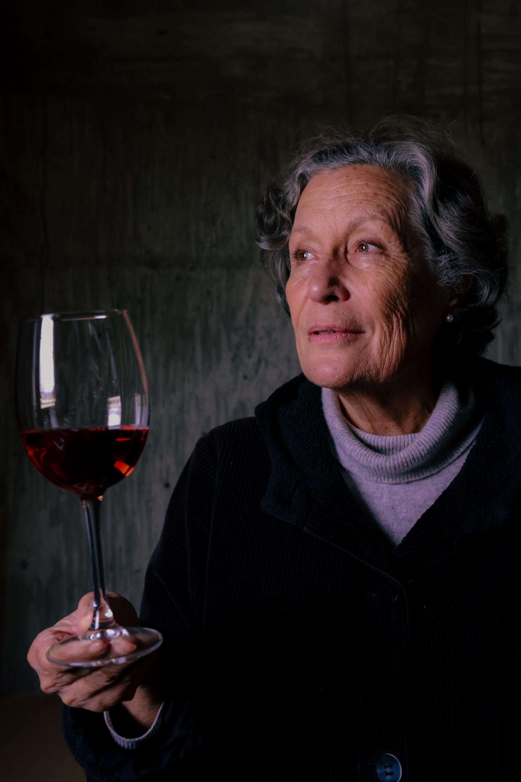 An older woman holding a wineglass of red wine by its base