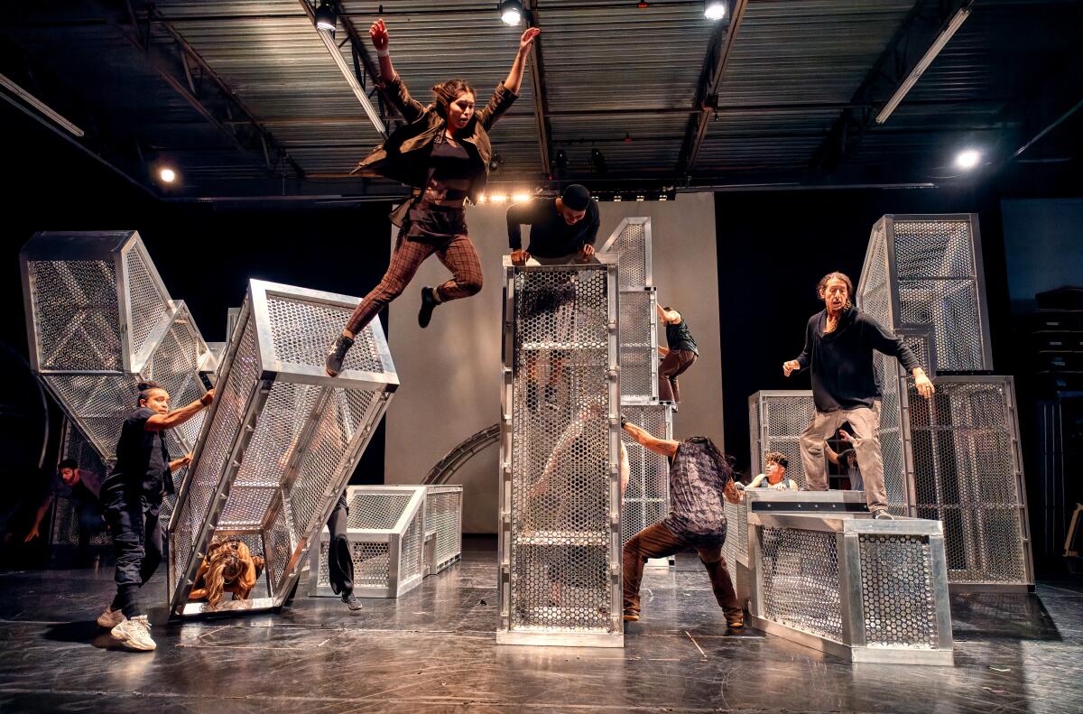 Dancers moving and jumping off metal set pieces on stage.