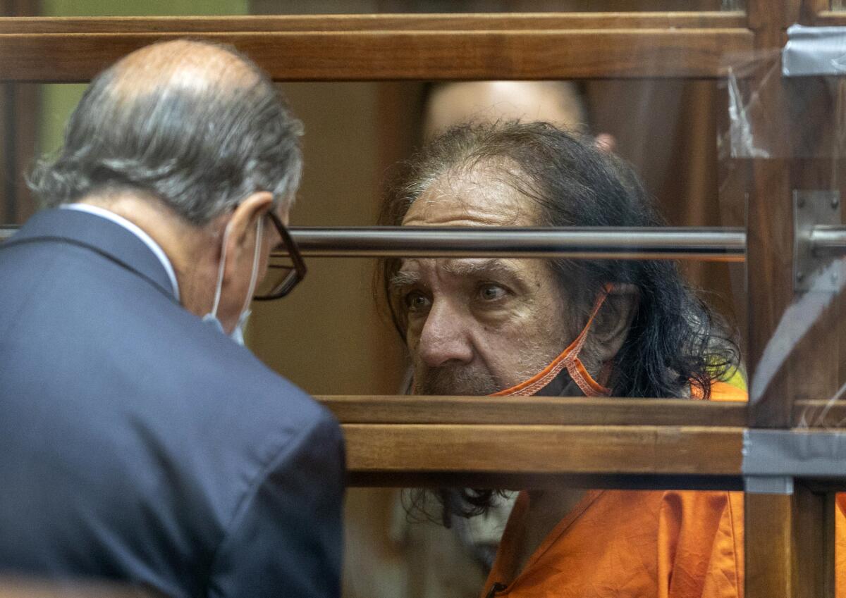 Adult film star Ron Jeremy, wearing a prison jumpsuit, talks with his attorney Stuart Goldfarb during his arraignment 