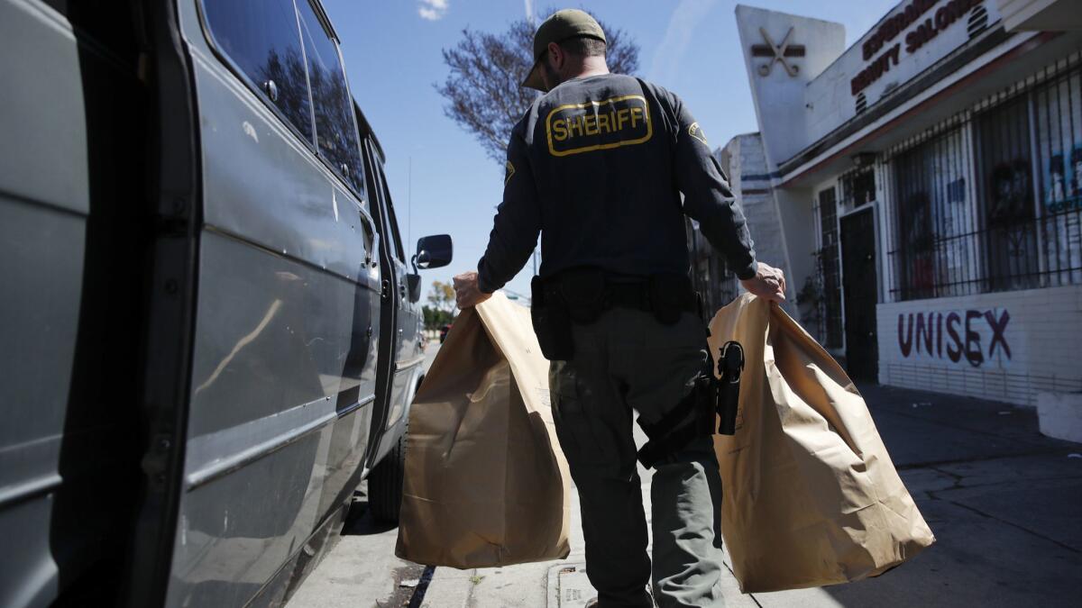 An undercover Los Angeles County sheriff's deputy loads two evidence bags into a van after raiding an illegal marijuana dispensary in Compton in 2018.