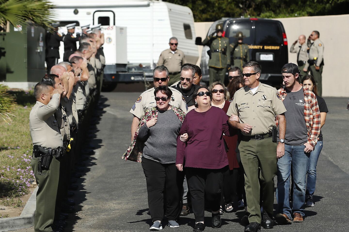Comdr. Christopher Dunn escorts relatives of Ventura County Sheriff's Sgt. Ron Helus as officers salute them near the entrance to the coroner's office.