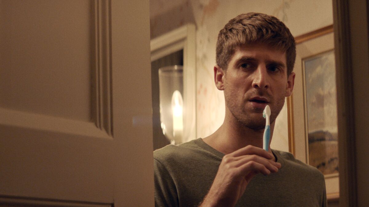 A man holding a toothbrush to his mouth in the movie “All My Friends Hate Me.”