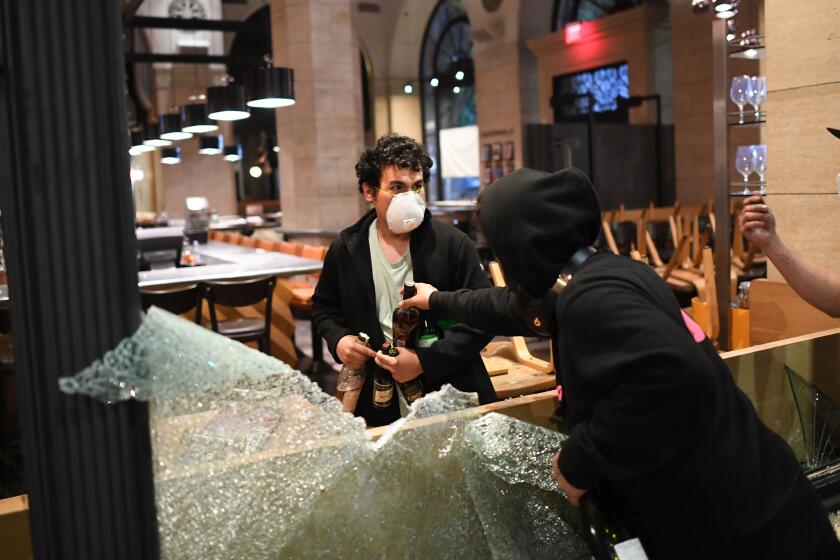 LOS ANGELES, CALIFORNIA MAY 29, 2020-A looter steals liquor bottles from Terroni restaurant on Spring St. in Downtown Los Angeles Friday. Protestors marched across the nation after the death of George Floyd. (Wally Skalij/Los Angeles Times)