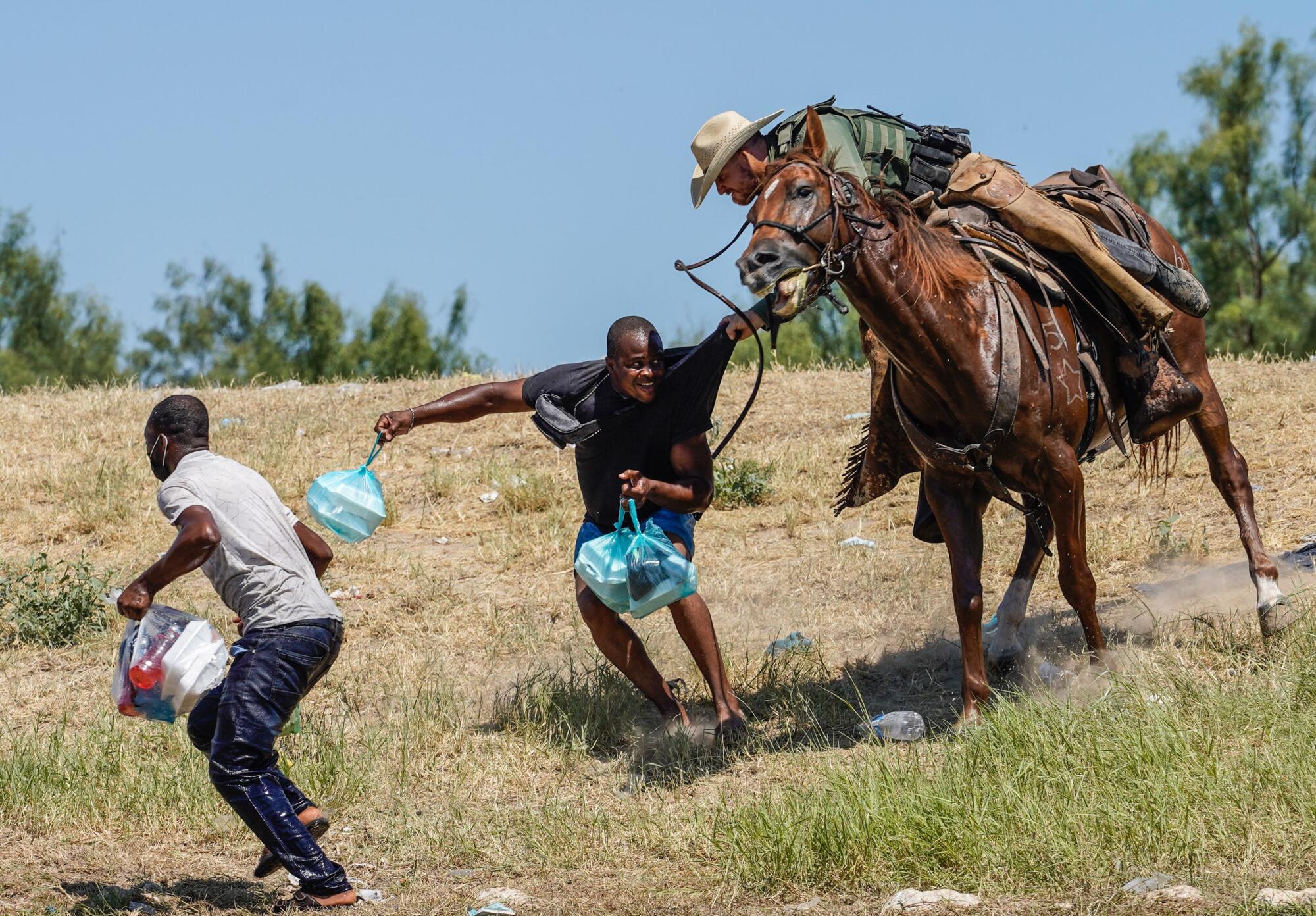 A Border Patrol agent on horseback tries to stop a Haitian migrant from entering an encampment.