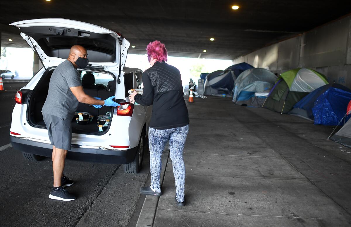 Tom Crump hands out free lunch to a homeless woman on Venice Boulevard under the 405 Freeway in Los Angeles on May 19, 2020. 