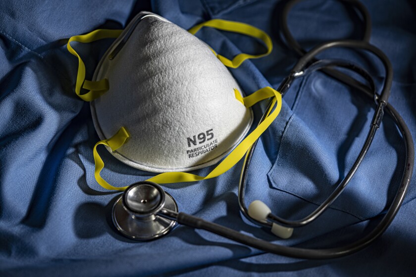 An N95 mask and a stethoscope on top of blue scrubs