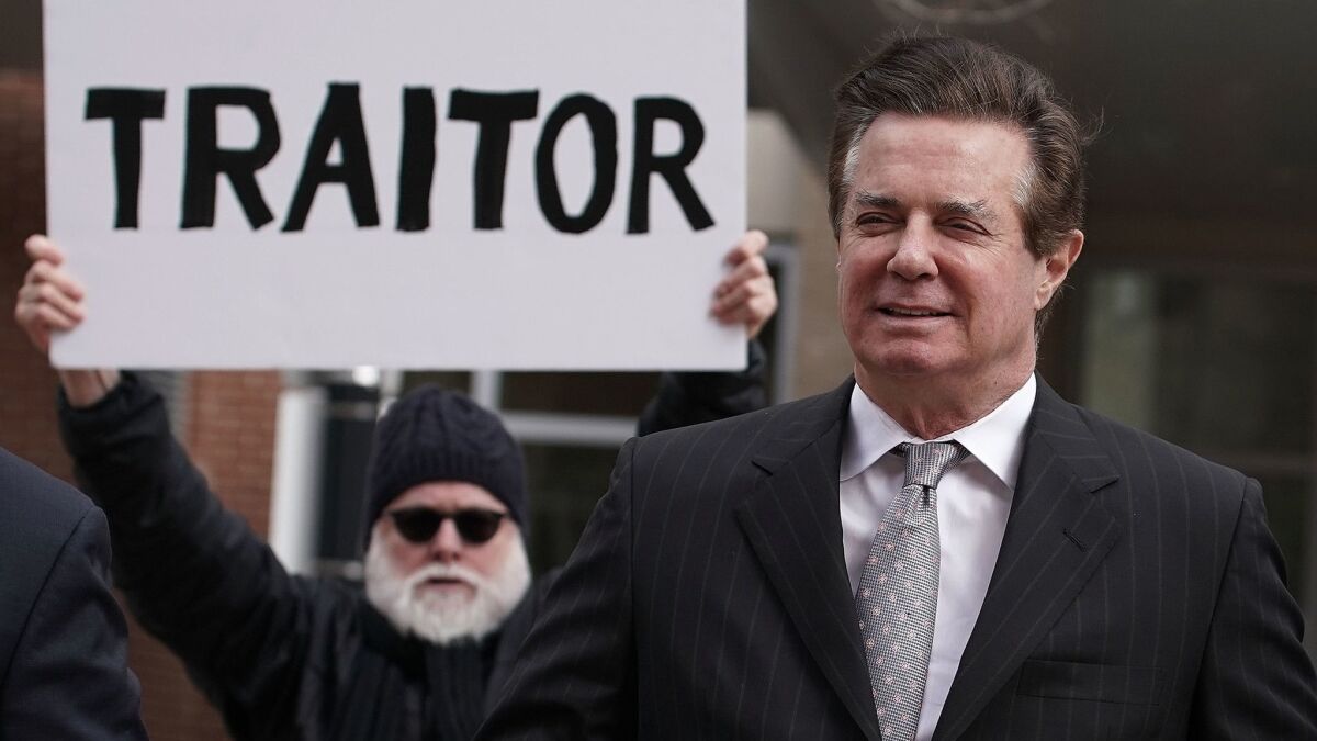 Former Trump campaign manager Paul Manafort (R) arrives at the Albert V. Bryan U.S. Courthouse for an arraignment hearing as a protester holds up a sign March 8, 2018 in Alexandria, Virginia.