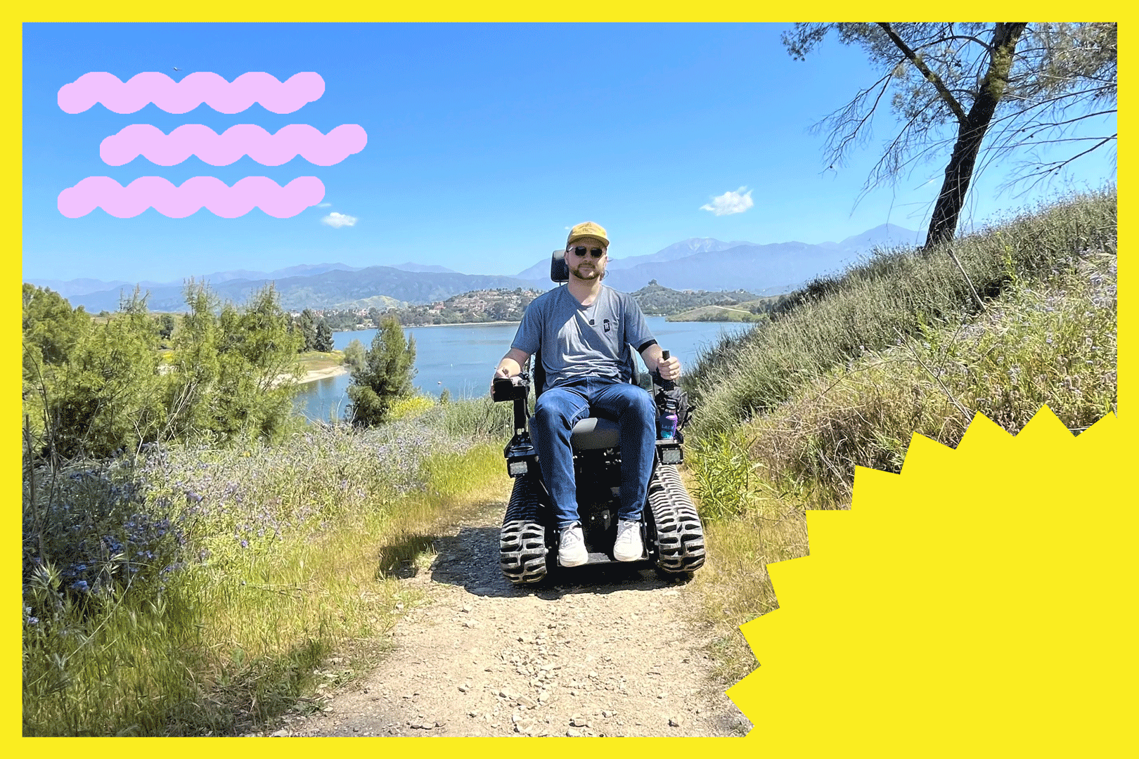 Photo of a man in an electric wheelchair on a hiking path beside a lake and a blue sky