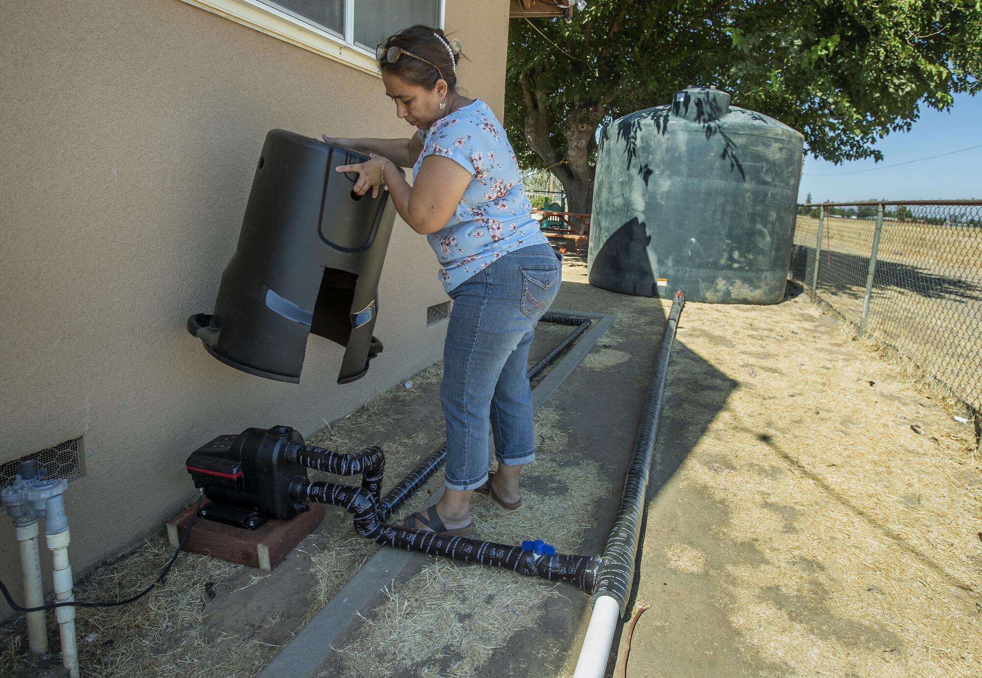 A woman lifts a container, showing pipes connected to a water tank