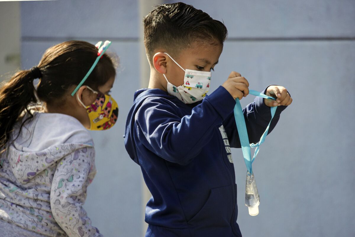 A boy wears face mask and carries a hand sanitizer bottle at Madison Elementary School  in South Gate.