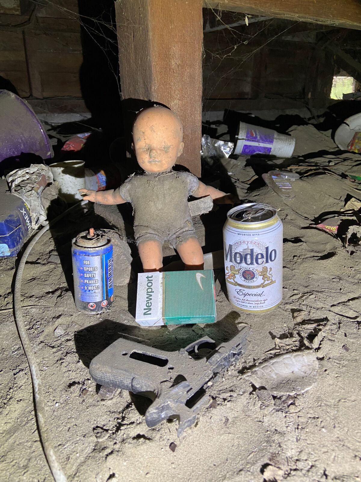 A doll, a beer can, a toy gun, a pack of cigarettes and other items in a crawl space.