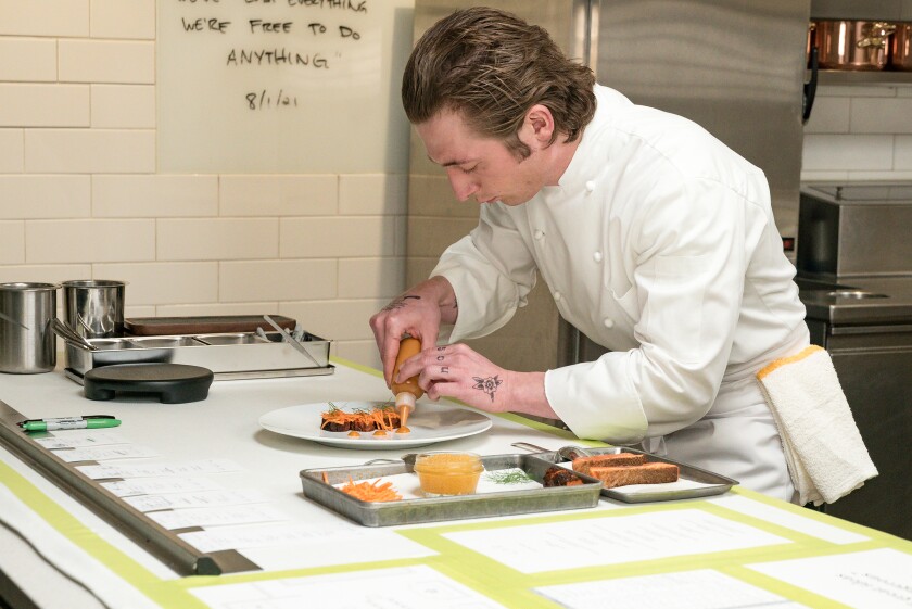 A man in a white coat puts orange sauce on a dish.