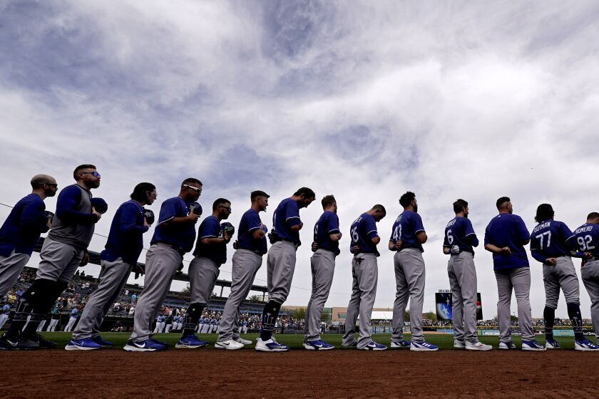 Dodgers players stand for the national anthem before a spring training game against the Seattle Mariners 