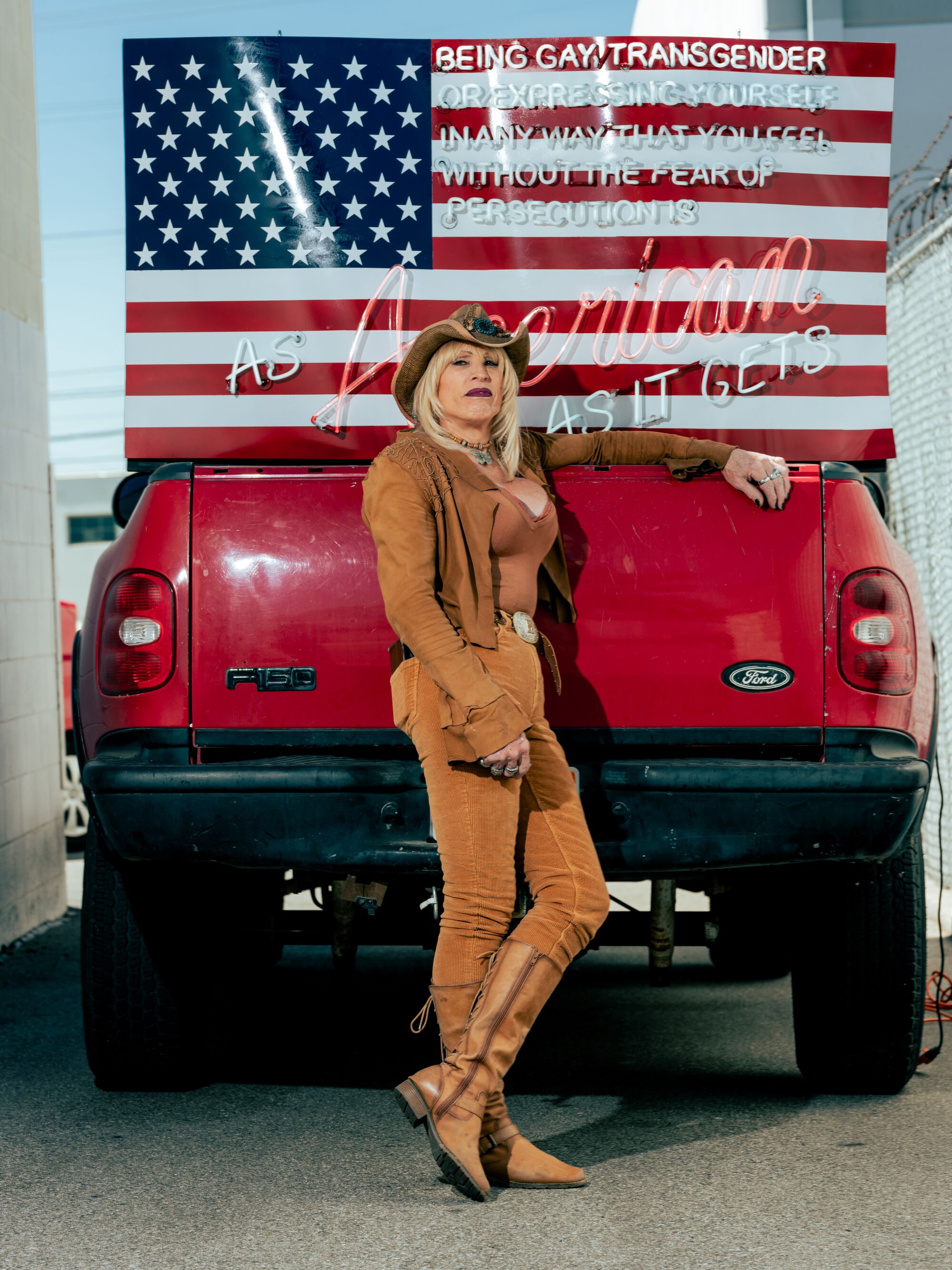 A woman in brown stands in front of a neon art piece incorporating the American flag