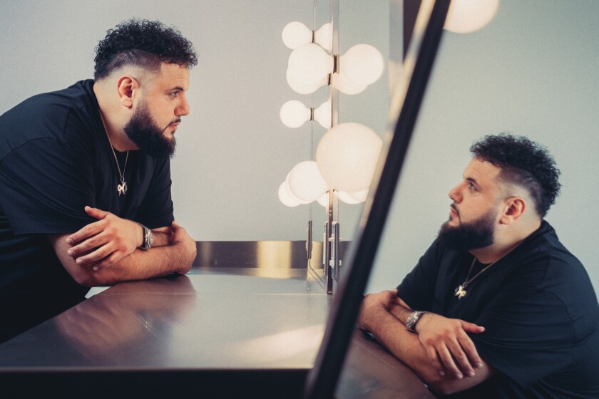 A man in a black T-shirt looks at himself in a mirror