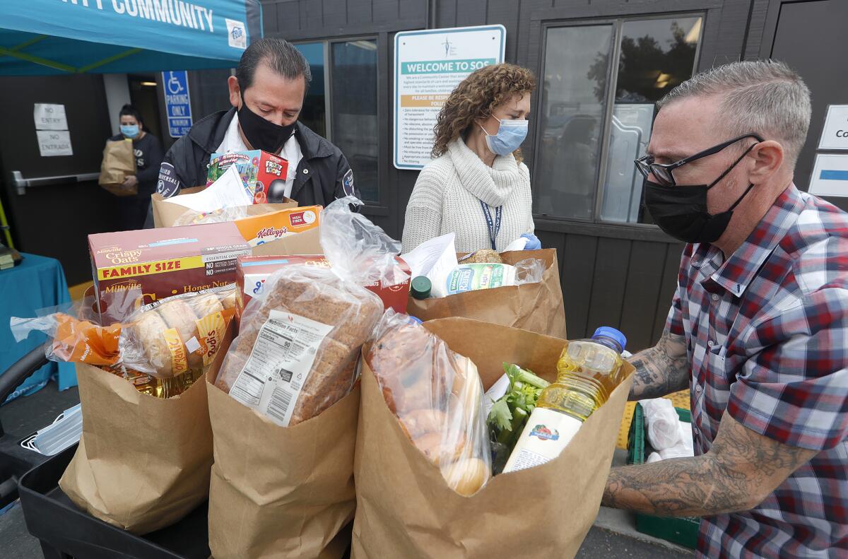 CEO Christy Ward, in white, and clinical case manager Ian Ashby, right, gather bags of groceries.
