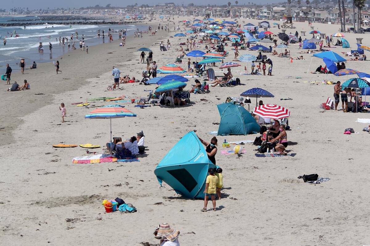 A woman folds up her tent as beachgoers hang out Friday in Newport Beach.