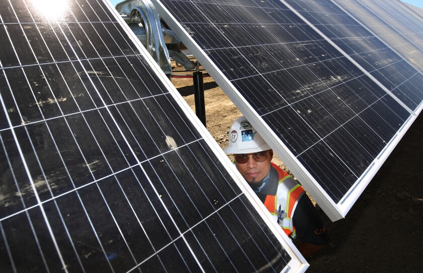 A man in a hardhat is seen between two sets of solar panels.