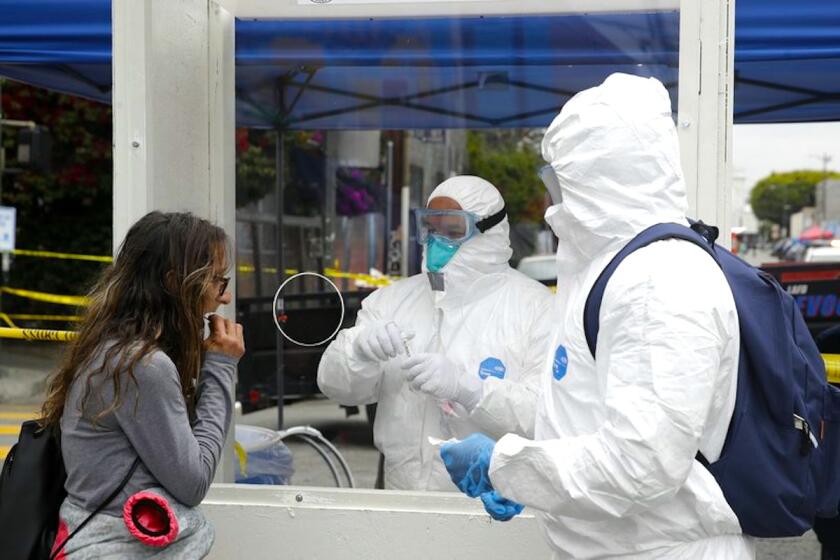 Elementos del Departamento de Bomberos con equipos de protección hacen una prueba de coronavirus a una mujer en el distrito de Skid Row, en Los Ángeles.
