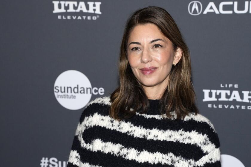 Sofia Coppola in a chunky black-and-white striped sweater posing in front of a gray background