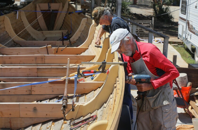 Two men put nails in a Viking boat.
