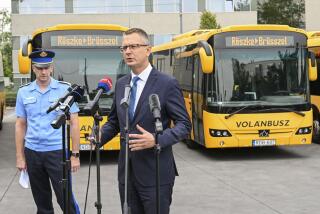 Hungary's State Secretary Bence Rétvári, right, and National Deputy Chief of Police Janos Kuczik hold a joint press conference at the bus station of Nepliget, Budapest, Hungary, Friday Sept. 6, 2024, backdropped by a row of passenger buses with illuminated signs reading “Röszke-Brussels” — a route that would take migrants from Hungary's southern border with Serbia to the EU headquarters in Belgium. (Tibor Illyes/MTI via AP)