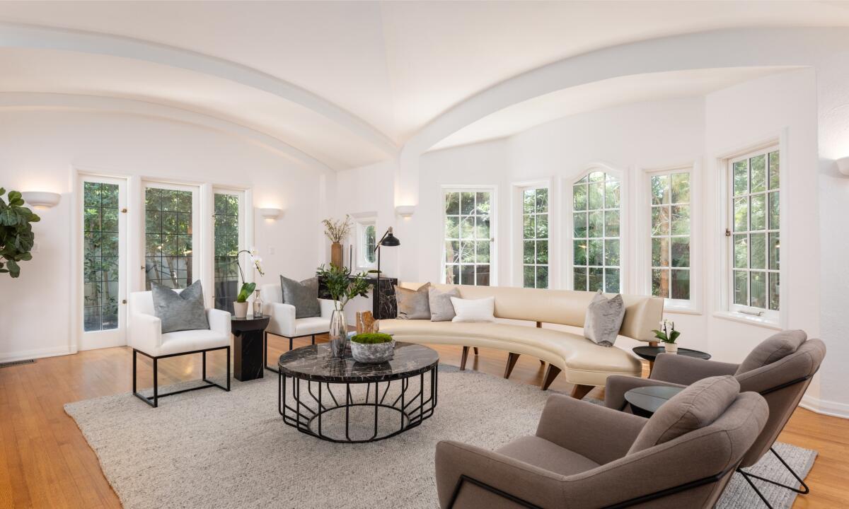 A room with a rounded sofa, chairs and a table in the middle with plants on it.