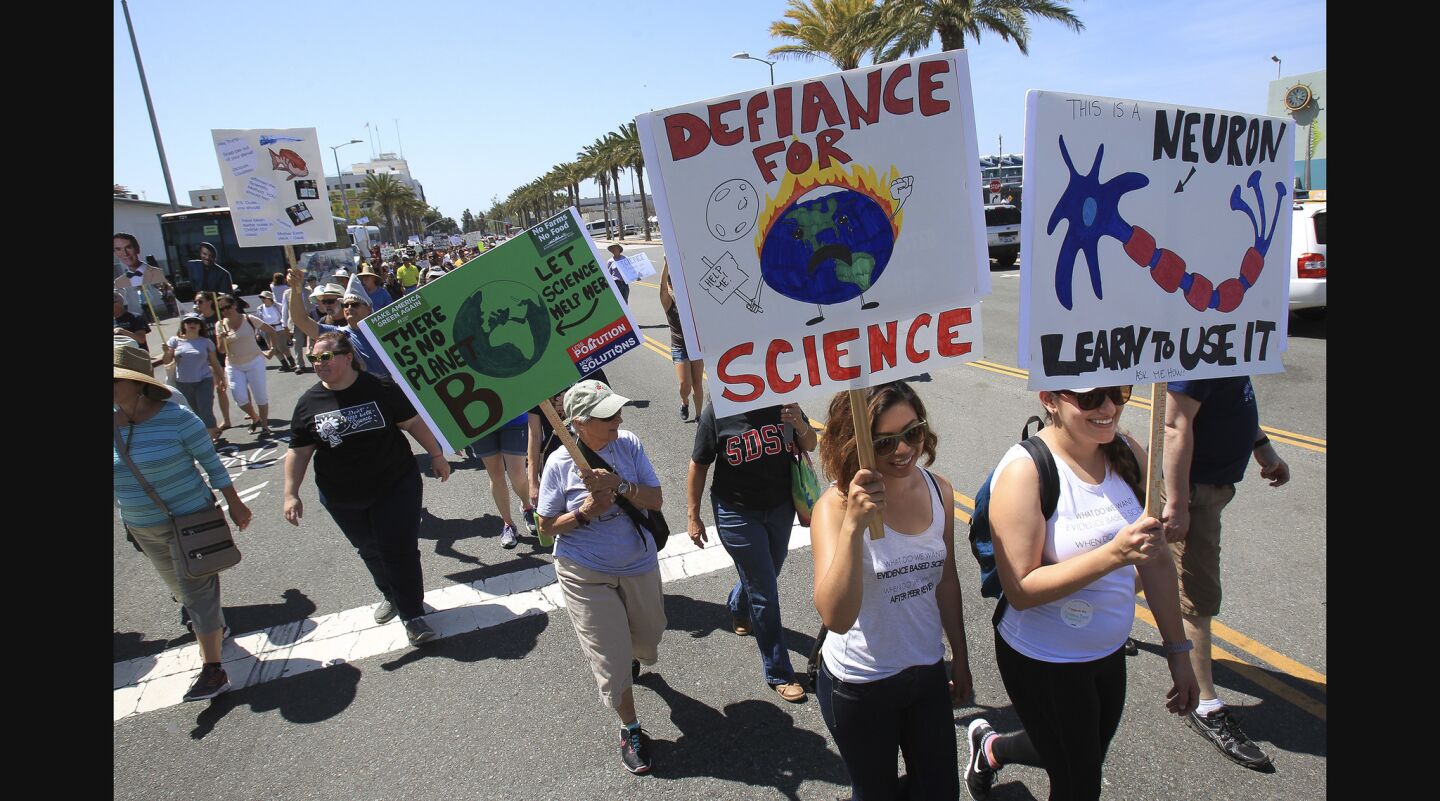 Raelynn Quiambao, front center, and Maya Ayalo, right, carry signs as they and other people participating in the March for Science walk down North Harbor Drive.
