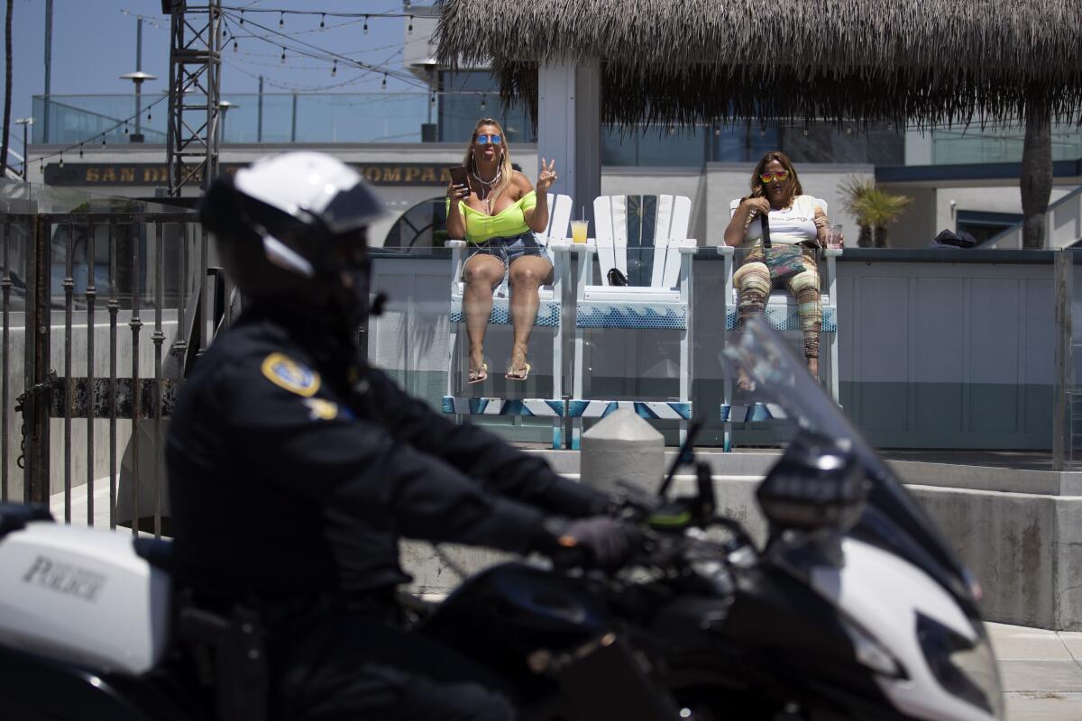 A police officer on a motorcycle passes two women drinking by a beach