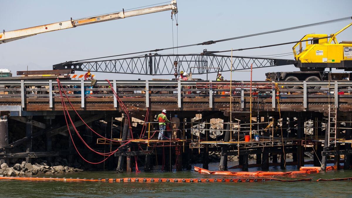 Orange County Public Works crews in 2015 work to repair a damaged bridge at Edinger Avenue in Huntington Beach. The county has started its work to replace the timber bridge with a concrete one.