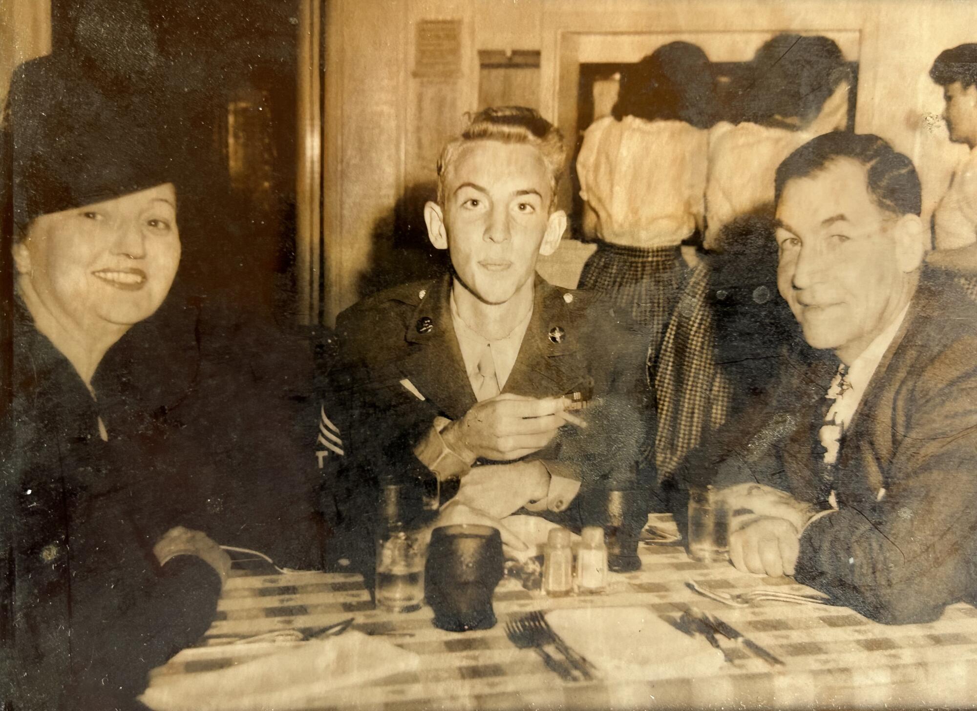 A young man seated between his parents in a vintage photo.