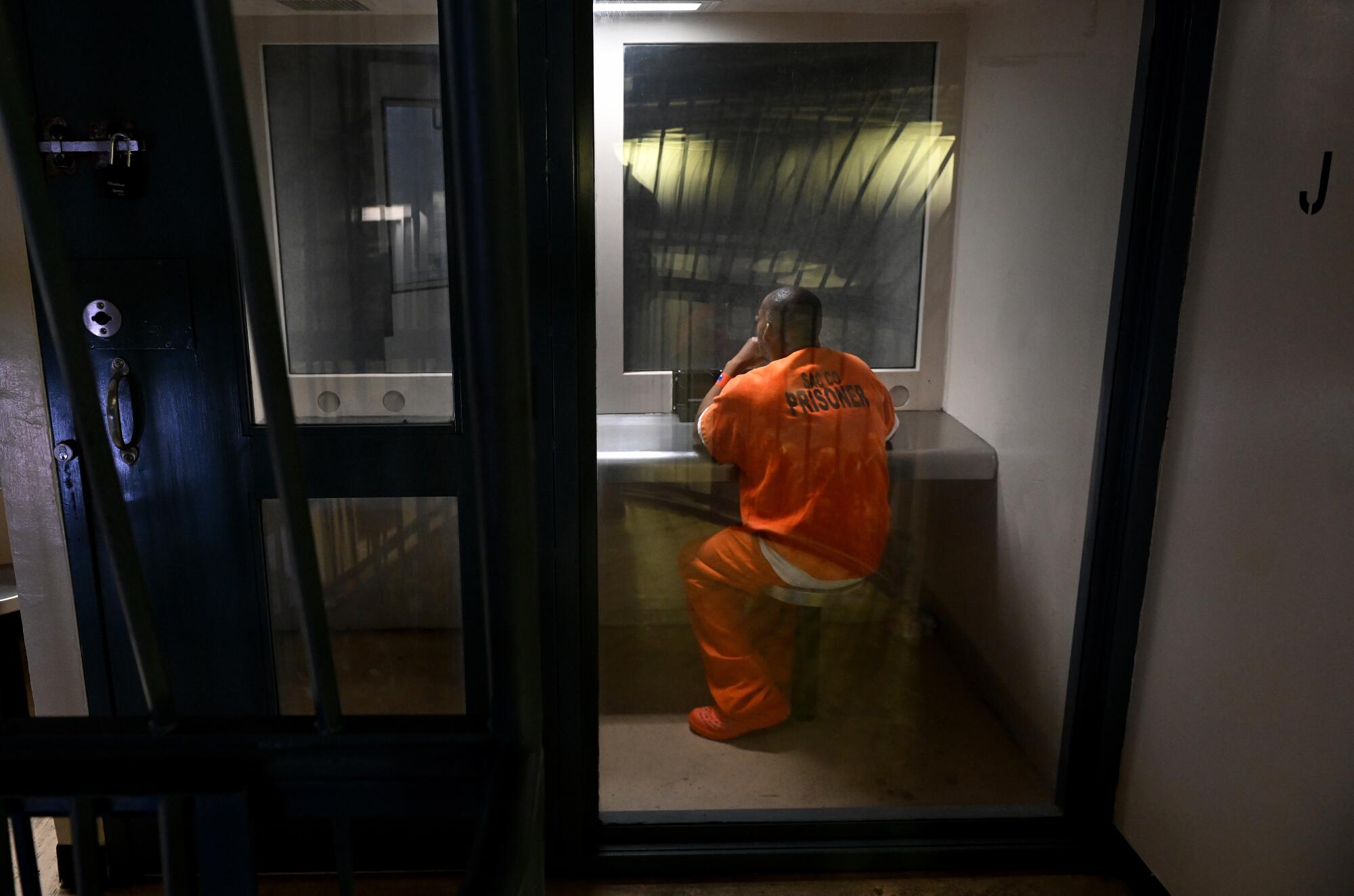 A Sacramento County jail inmate sits in a booth to talk on the phone.