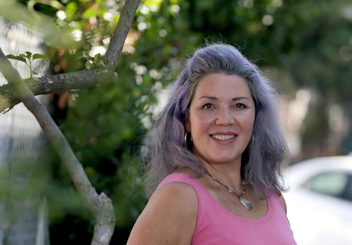 A woman in a sleeveless pink top stands in front of a tree smiling for a photo.