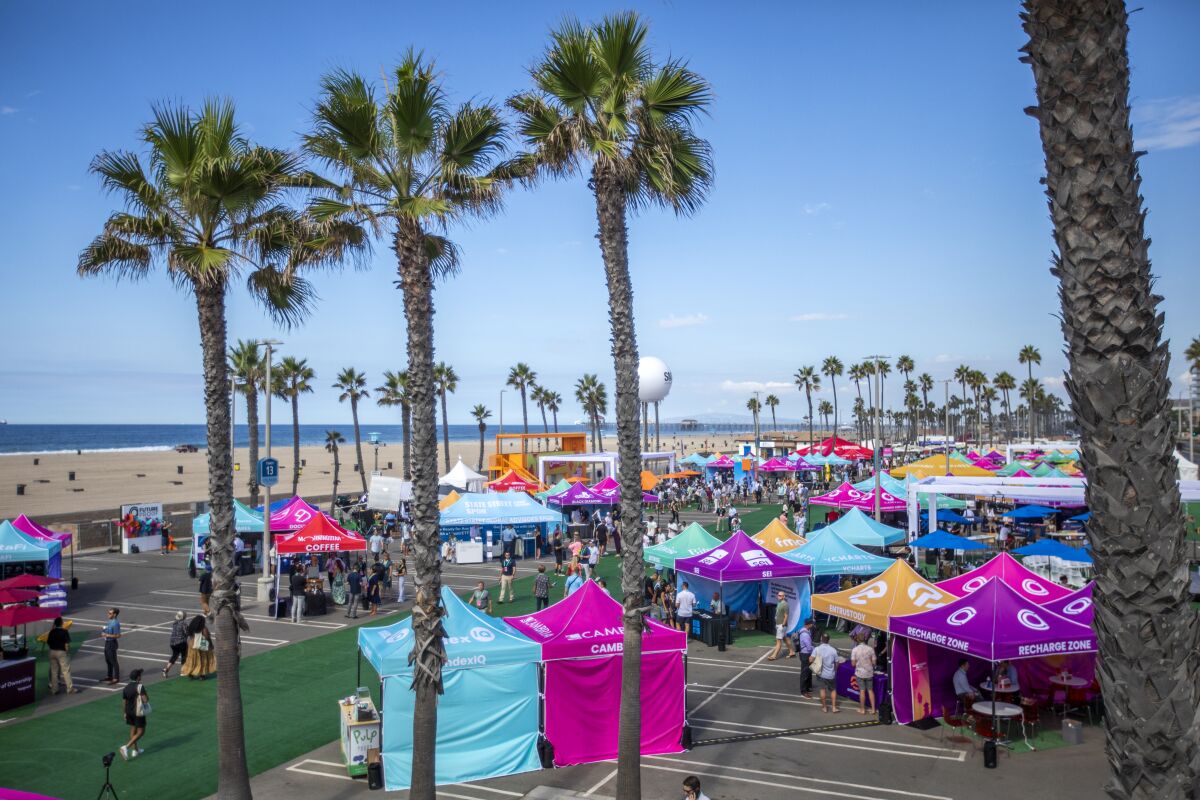 People mingle under and around colorful tents in a beachside parking lot.