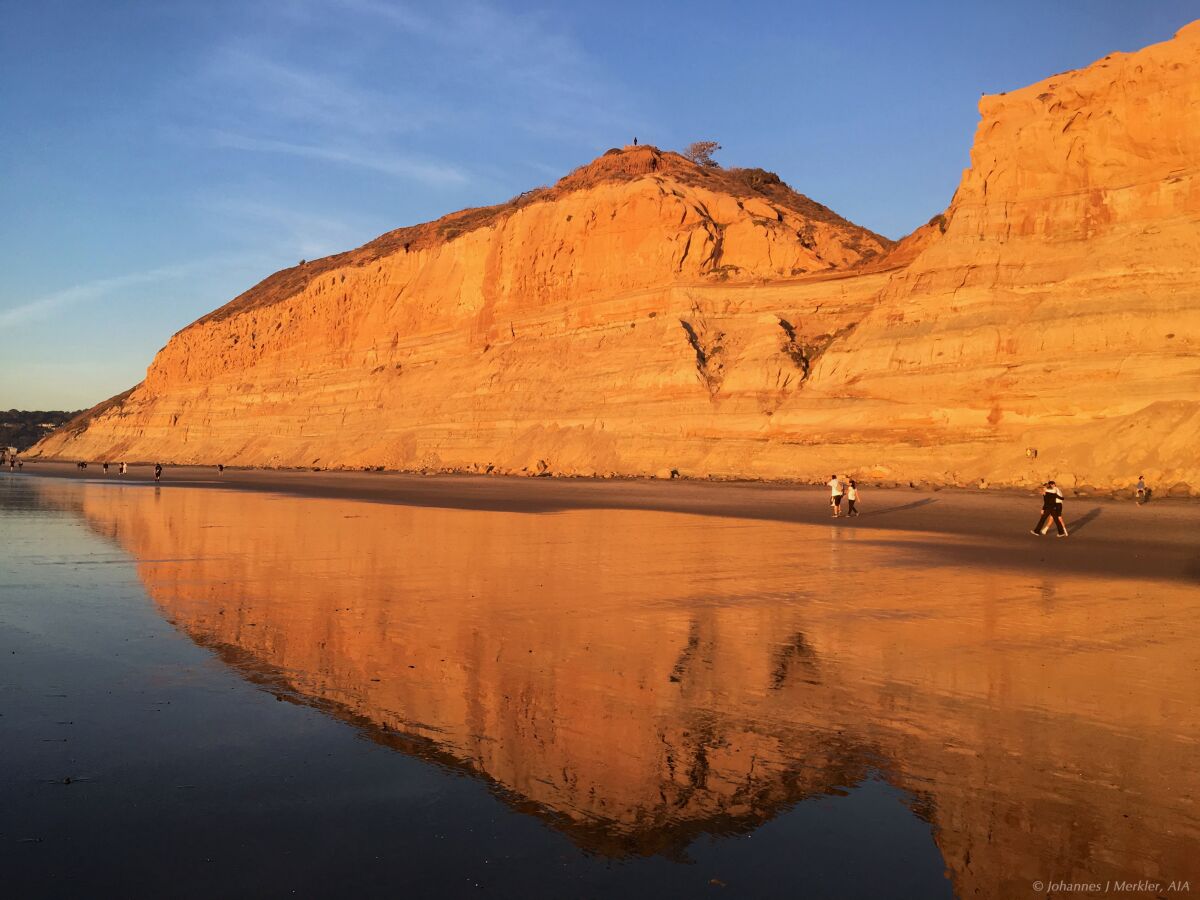 A large rock face on a beach with people walking below it.