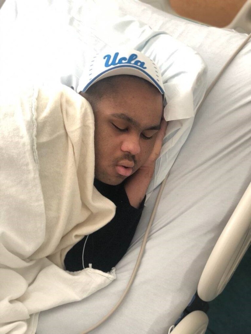 Luke Forbes schläft in einem Krankenhausbett, während er einen UCLA-Hut trägt 