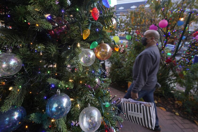 A pedestrian carries a bag past holiday decorations outside of Just for Fun & Scribbledoodles store during the coronavirus pandemic in San Francisco, Wednesday, Dec. 23, 2020. (AP Photo/Jeff Chiu)