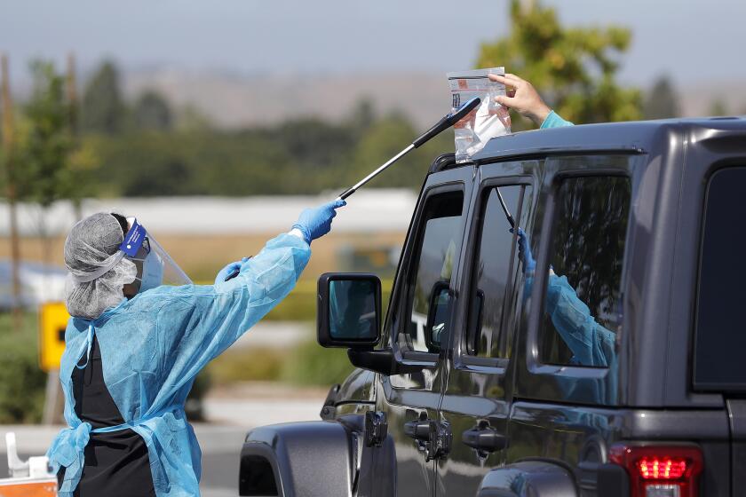 Health specialist Mari Cruz grabs a completed test from a motorist during drive-up COVID-19 testing for individuals who live in Irvine at the Orange County Great Park on Monday.