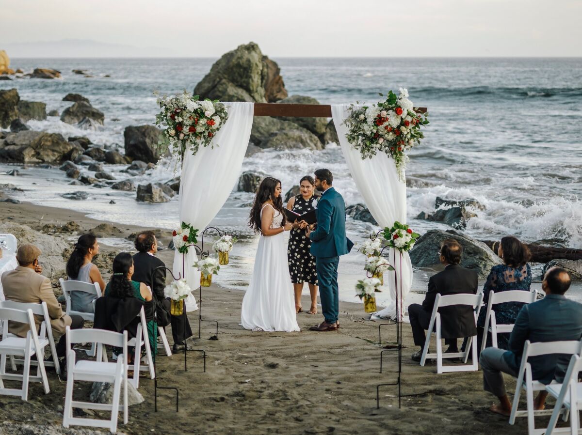 This photo shows bride Namisha Balagopal and groom Suhaas Prasad getting married in a small legal ceremony Aug. 15, 2020, on Muir Beach near San Francisco. The couple plans a larger traditional South Asian Indian wedding this August in Utah amid a boom in post-vaccination nuptials around the world. (Vellora Productions via AP)