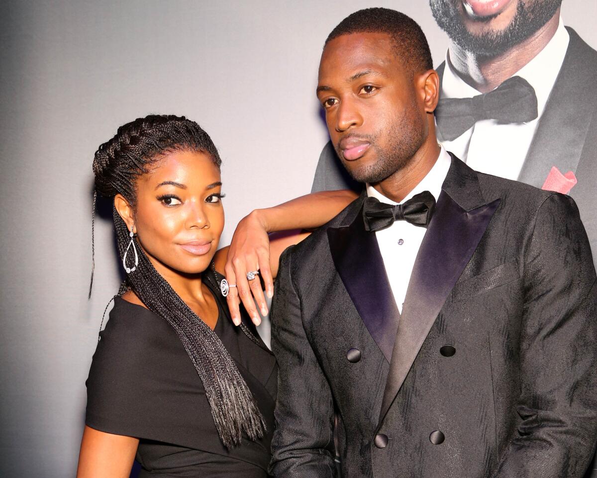 Gabrielle Union, in a black dress and dangling earrings, leans an arm on the shoulder of Dwyane Wade, in a tux.